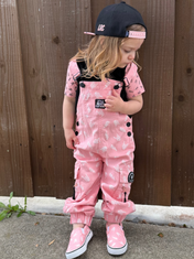 young girl wearing pink overalls with rock on horns and lightening bolts from little rocker clothing