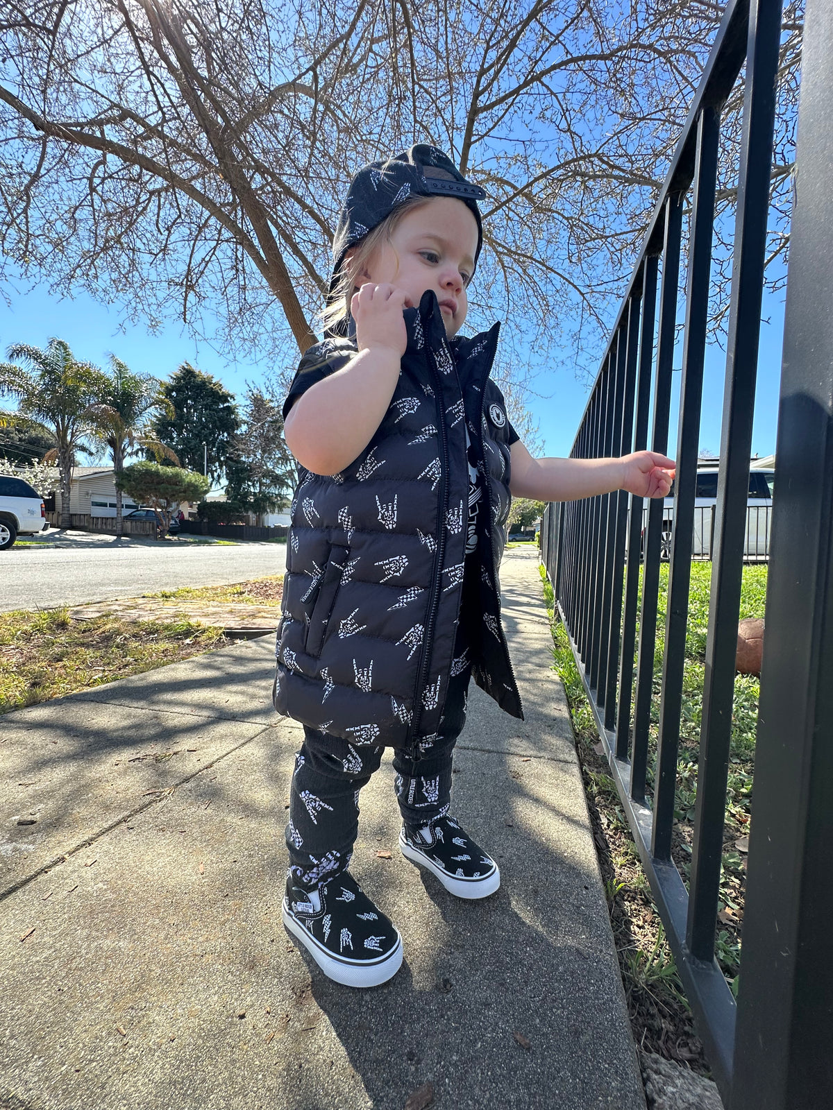 girl outside wearing the  Kids black puffer vest with Bolted Bones design featuring skeleton hand rock on graphic and lightning bolts, rocker style outerwear for kids