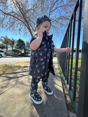 girl outside wearing the  Kids black puffer vest with Bolted Bones design featuring skeleton hand rock on graphic and lightning bolts, rocker style outerwear for kids