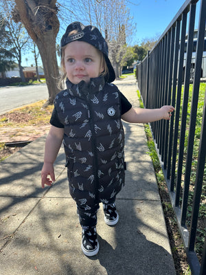 Toddler girl wearing Kids black puffer vest with Bolted Bones design featuring skeleton hand rock on graphic and lightning bolts, rocker style outerwear for kids