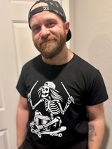 adult man wearing a black graphic tshirt featuring a skeleton sitting on a skateboard with drumsticks 