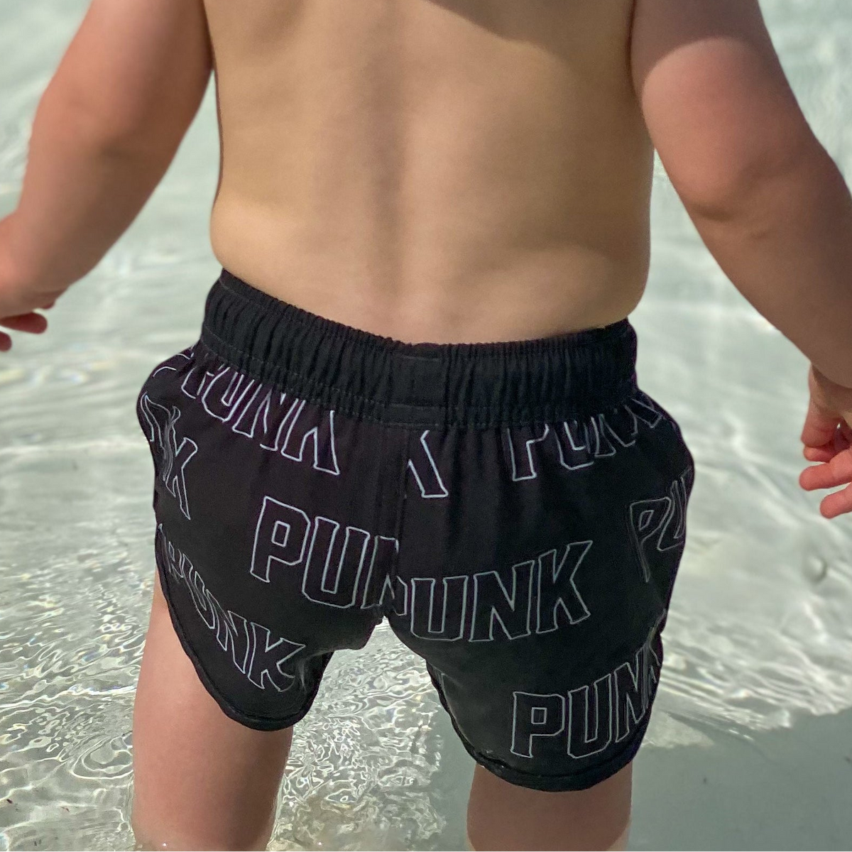 infant wearing black swim trunks with punk pattern