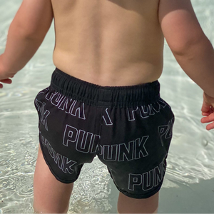 infant wearing black swim trunks with punk pattern