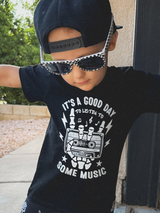 black kids graphic t-shirt with skeleton hands holding cassette tape and “it’s a good day to listen to some music” text, little rocker clothing rock style outfit with checkered sunglasses and snapback front view