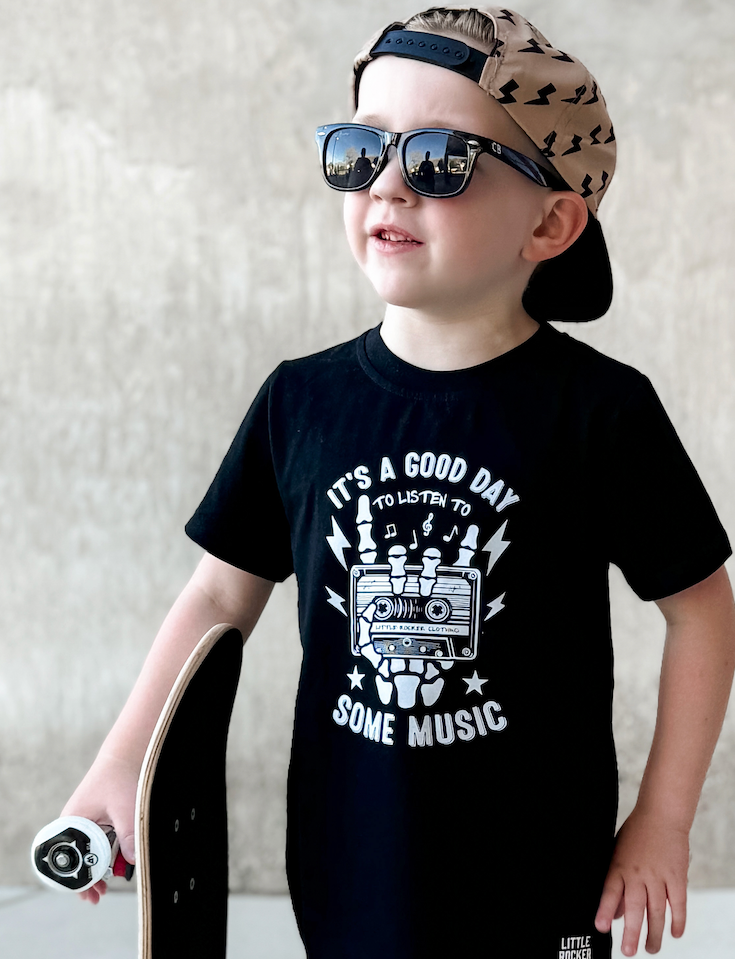 black kids graphic t-shirt with with it's a nice day to listen to some music, little rocker clothing punk rock toddler outfit front view smiling child outdoors